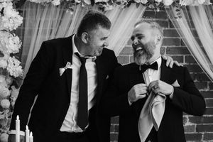 Four black and white photos show wedding moments and groomsmen sharing laughter amidst brick wall and curtain backdrops.