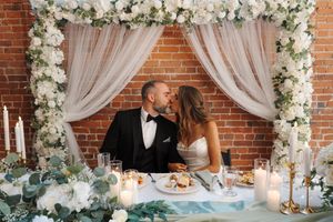 A romantic wedding reception dining area with brick walls, white floral arrangements, and sheer drapery decor.