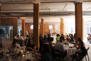 A panoramic view of people seated at tables in a dining event space with warm lighting and industrial ceiling details.