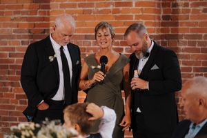 People gathering at a wedding reception with exposed brick walls, sharing laughter and conversation during speeches.
