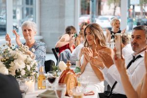 Wedding guests celebrate and applaud during a reception dinner with elegant floral centerpieces on the table.
