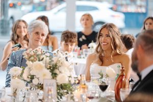 Wedding reception guests laugh and socialize at elegant tables decorated with white floral centerpieces and glassware.