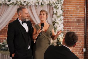 Wedding guests on dance floor with brick wall and floral decorations in background at evening celebration party.