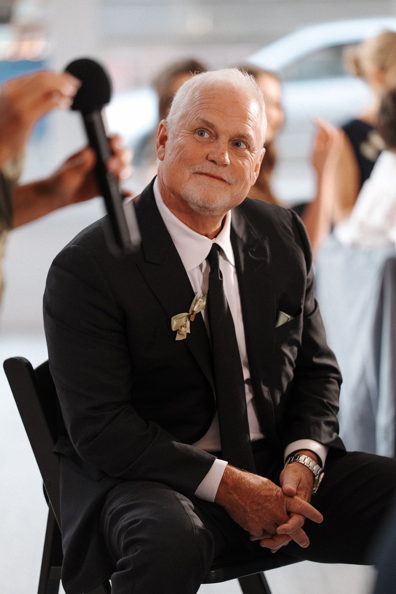 Professional looking well-dressed person in dark suit and tie sitting during a formal event or interview.