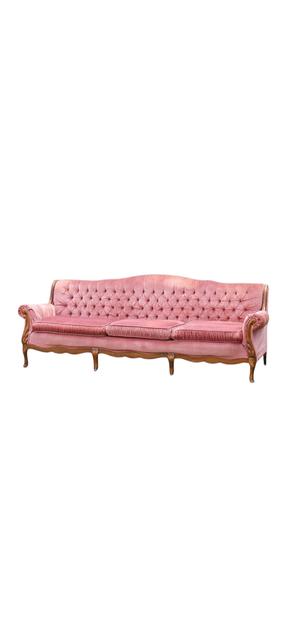 Vintage pink tufted velvet sofa with ornate wooden frame sits on grass against green foliage background.