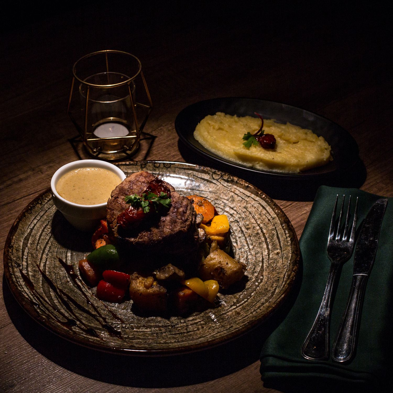 Elegant plated dinner dishes in moody lighting on textured placemats.
