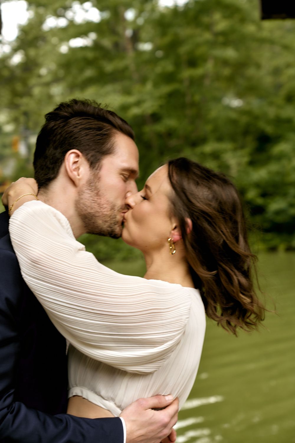 A romantic wedding couple sharing a passionate kiss outdoors with green foliage in the background. Wedding photoshoot