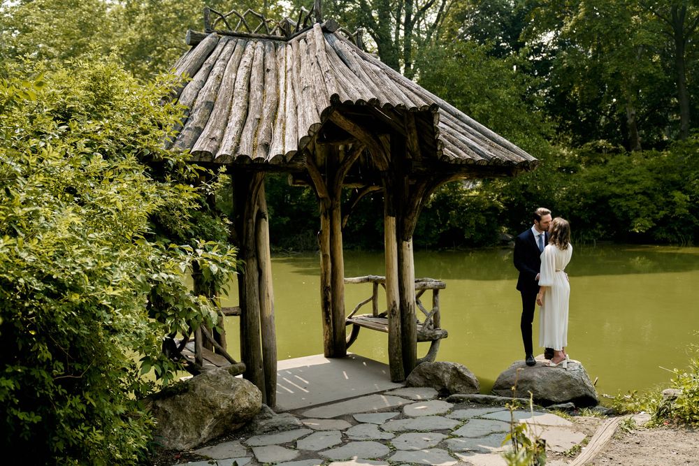 A bride and groom share a romantic moment under a wooden gazebo in a lush garden setting. Wedding photoshoot