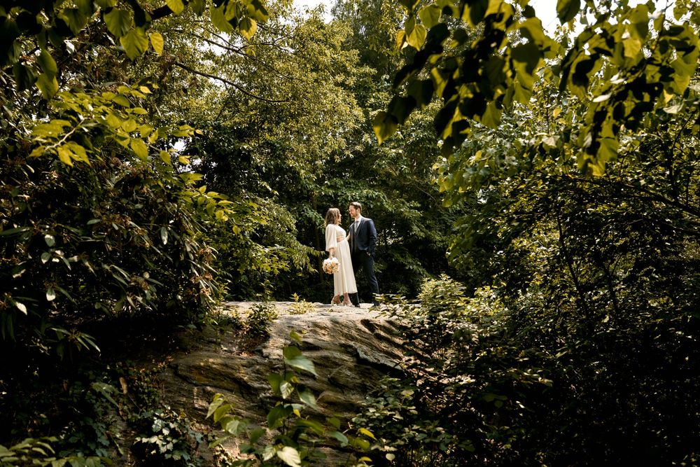 A person in white walking along a winding garden path surrounded by lush green foliage and flowers on a sunny day. Wedding photoshoot