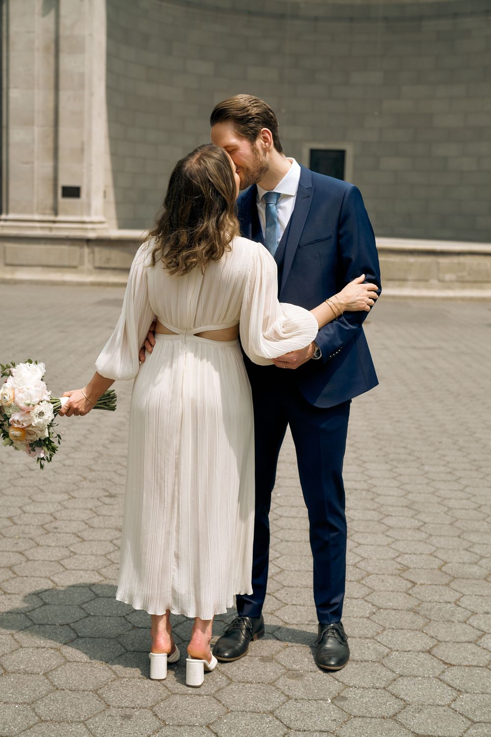Close-up of bride and groom wearing white dress and navy suit standing on hexagonal paving stones. Wedding photoshoot