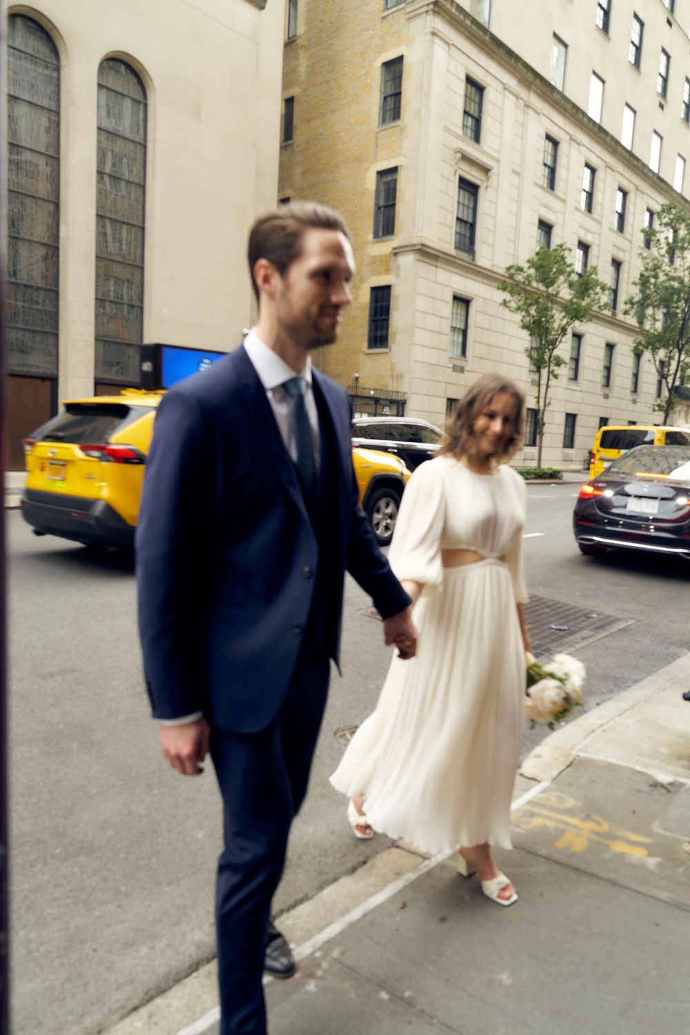 A bride and groom walking down a city street in formal attire. Wedding photoshoot