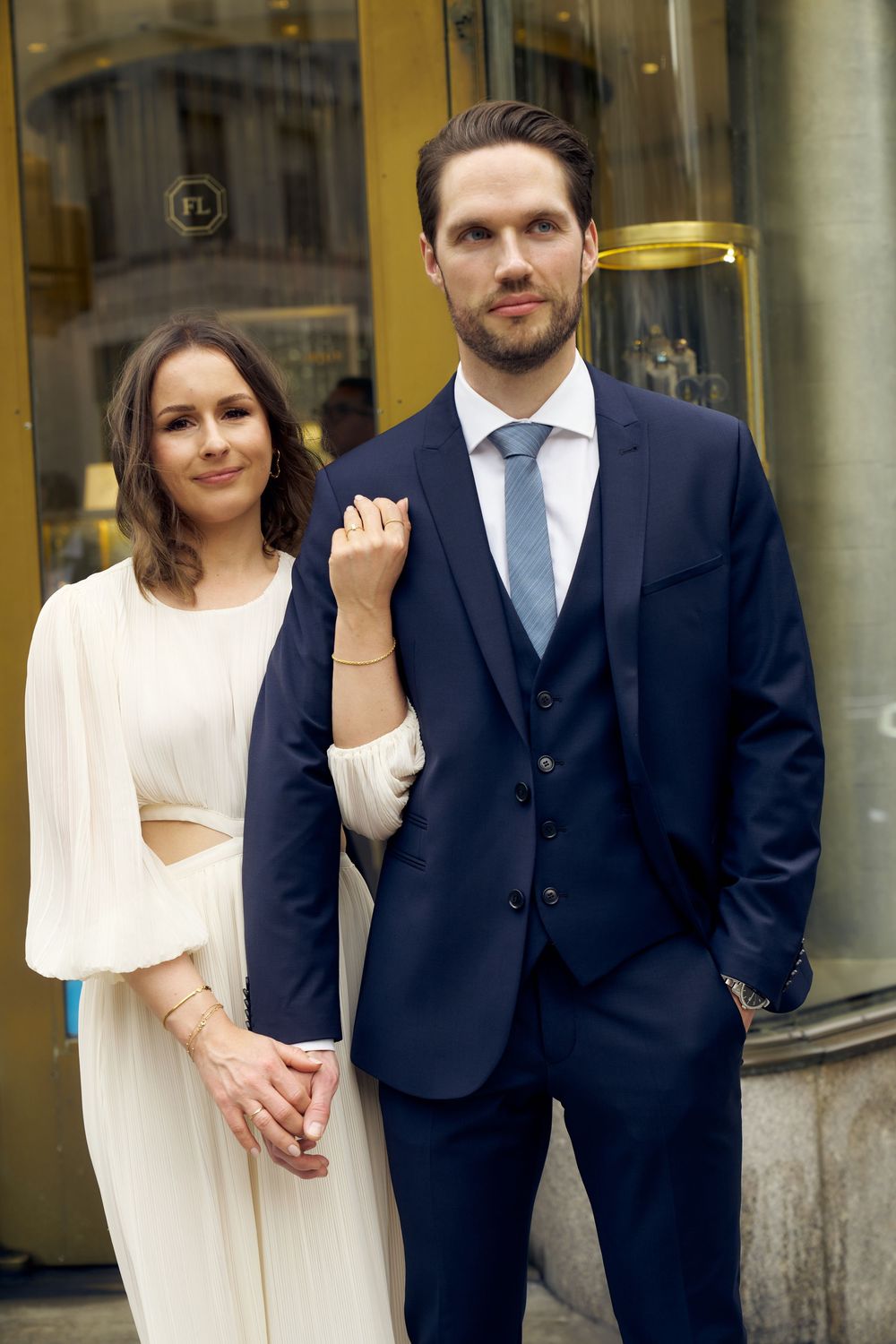 A couple poses together at a formal event, with the woman wearing a white dress and man in a navy suit. Wedding photoshoot