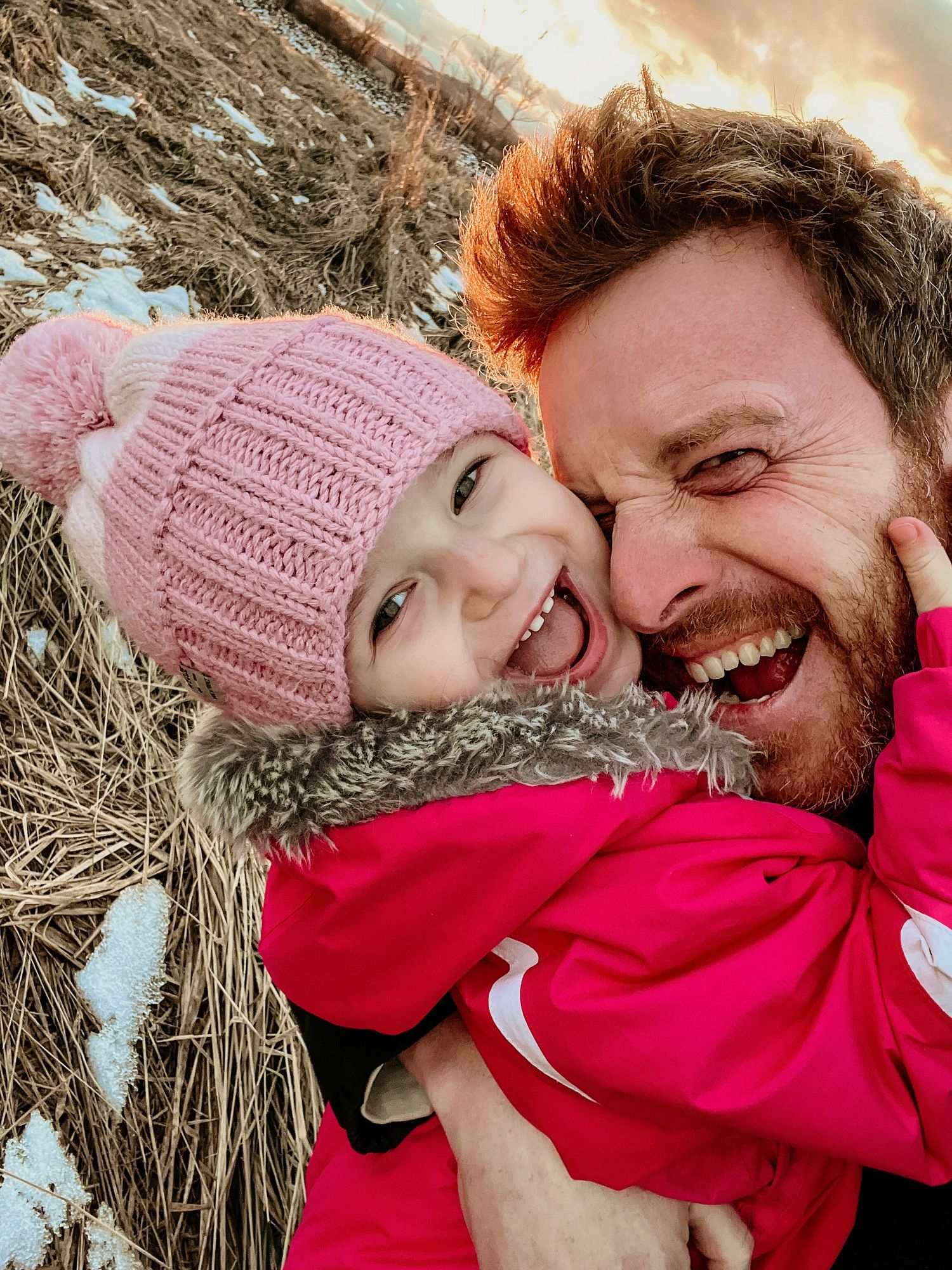 Cozy winter portraits showing warm embraces and pink knit hats against hay bales.