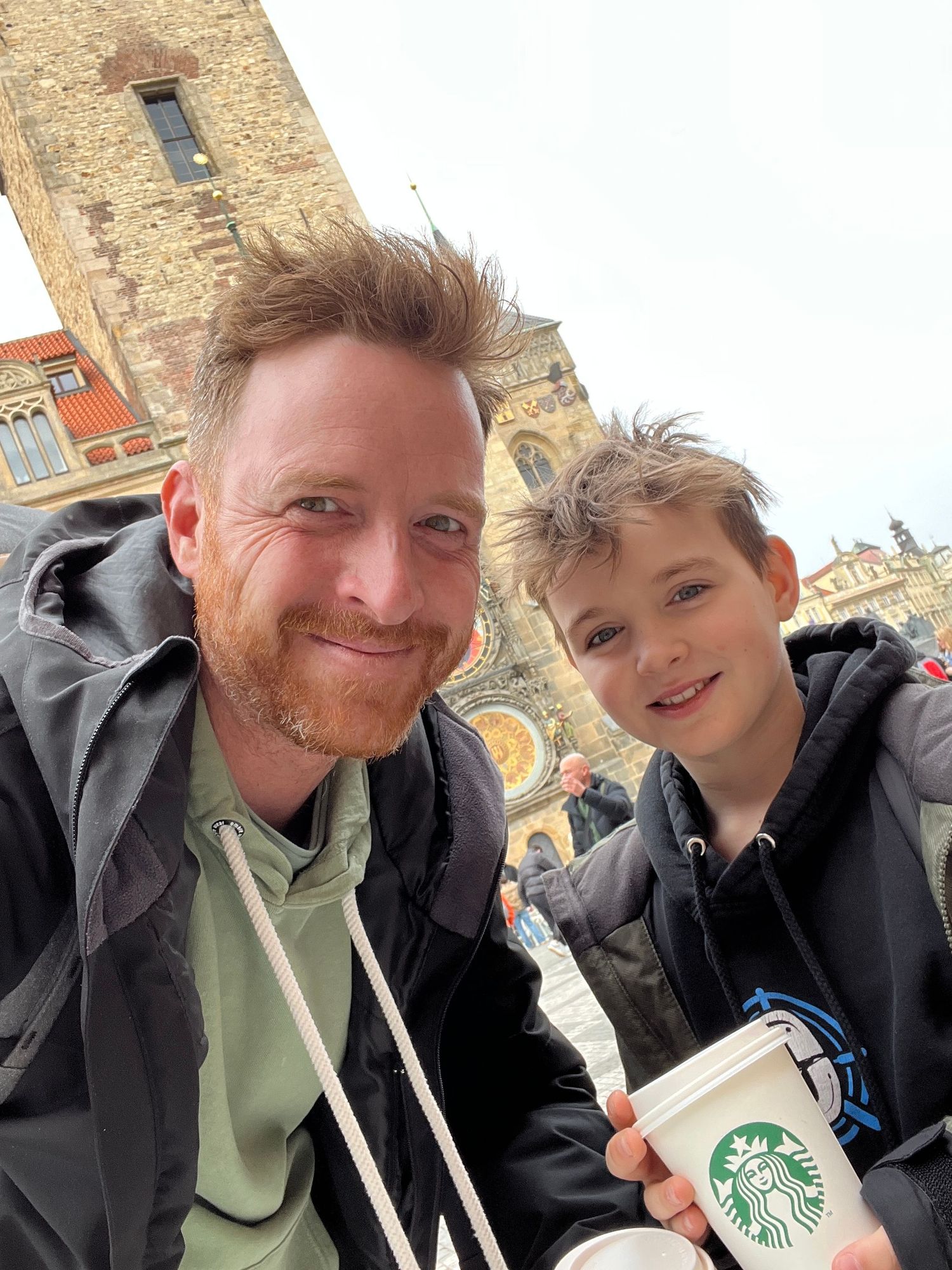 Two people sharing Starbucks drinks and smiling outside a historic building.