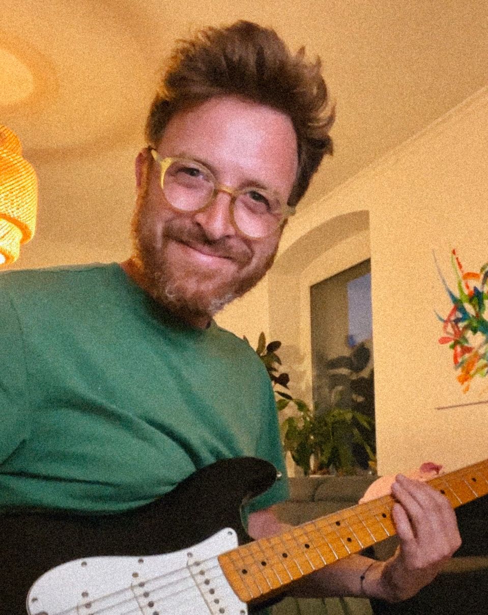 Musician plays electric guitar in warm-lit home studio setting.