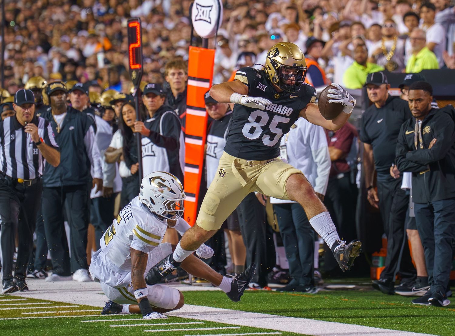 A dramatic American football play shows players diving and reaching for the ball near the sideline during a game.