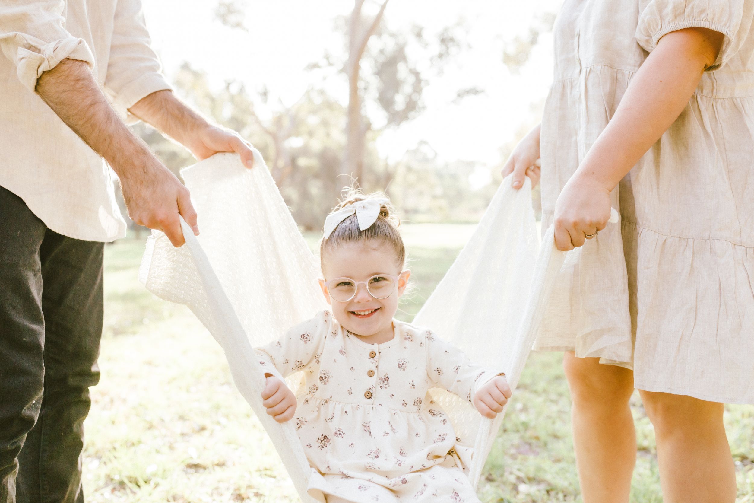 Young couple and toddler holding hands while walking through sunlit garden during family photoshoot.