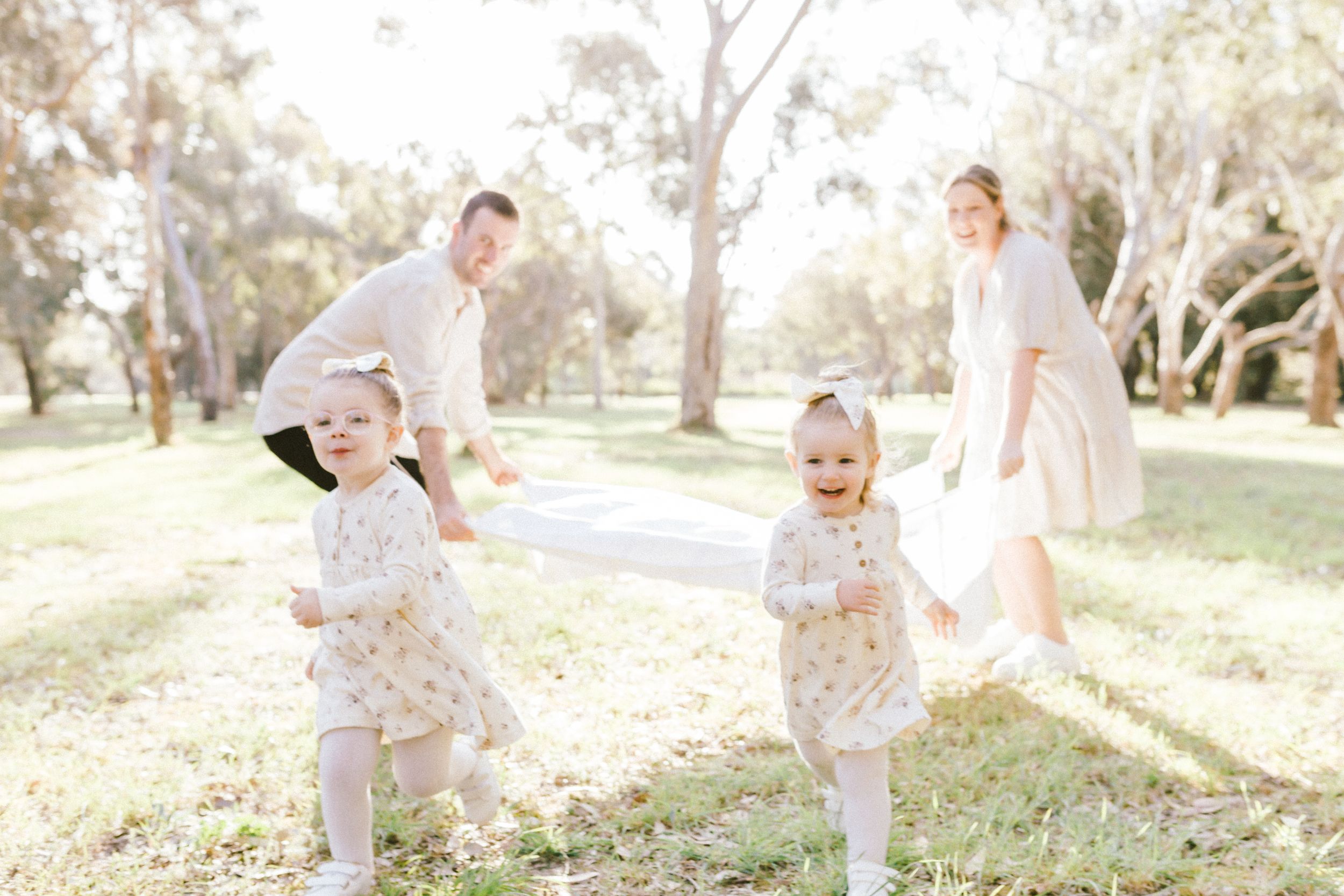 Family playing together on a sunny day in a park with sunlit trees in the background.