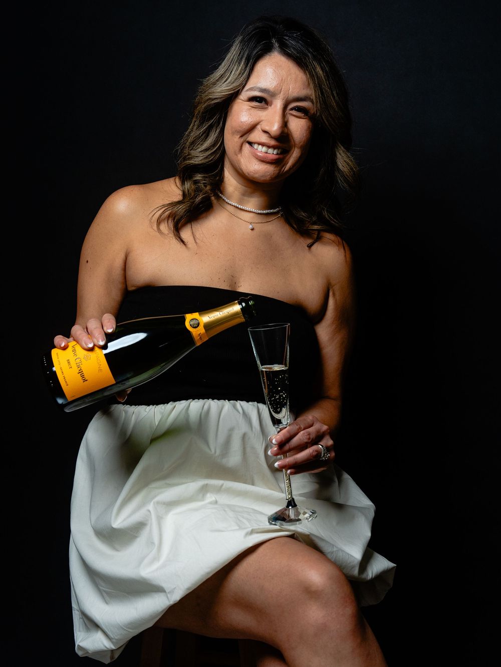 A series of four photos showing someone in a white off-shoulder top pouring and enjoying champagne against a dark background.