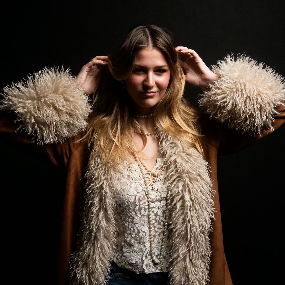 Person wearing a fluffy cream-colored feather boa poses against dark background in dramatic lighting.