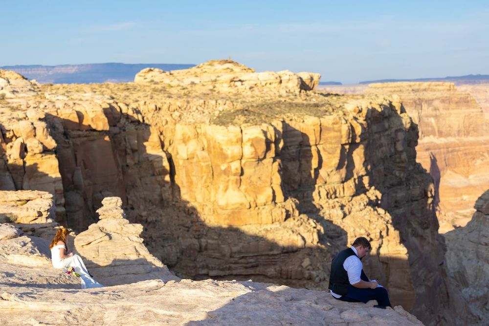 Person sits on rocky ledge overlooking majestic orange cliffs and canyons at Arches National Park during sunset.