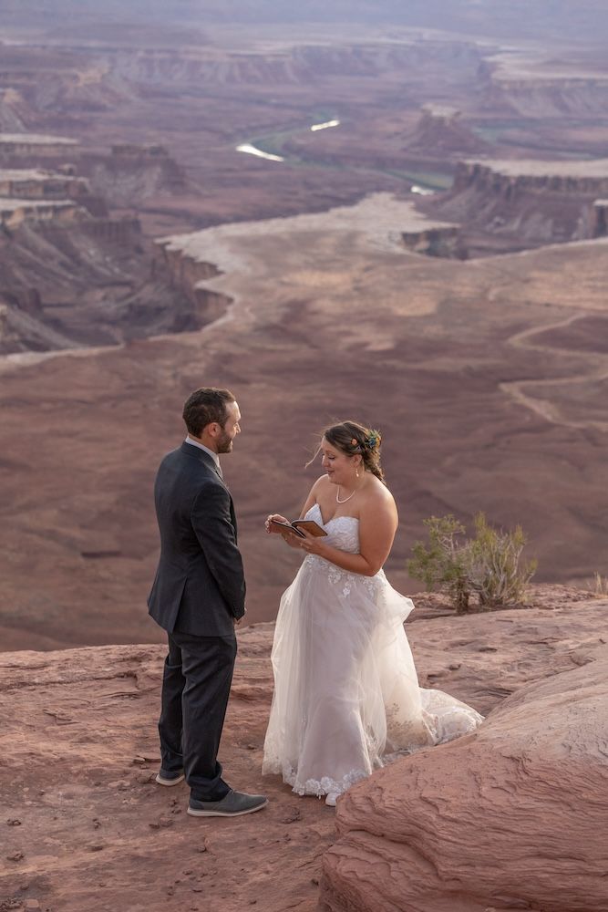 A couple in wedding attire shares a tender moment on the edge of a scenic desert canyon overlook.