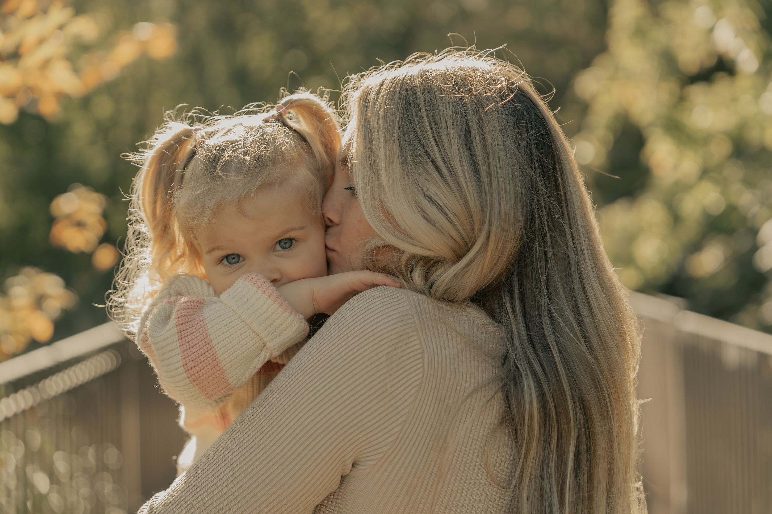 Parent and child share tender embrace in golden outdoor setting with warm autumn lighting.