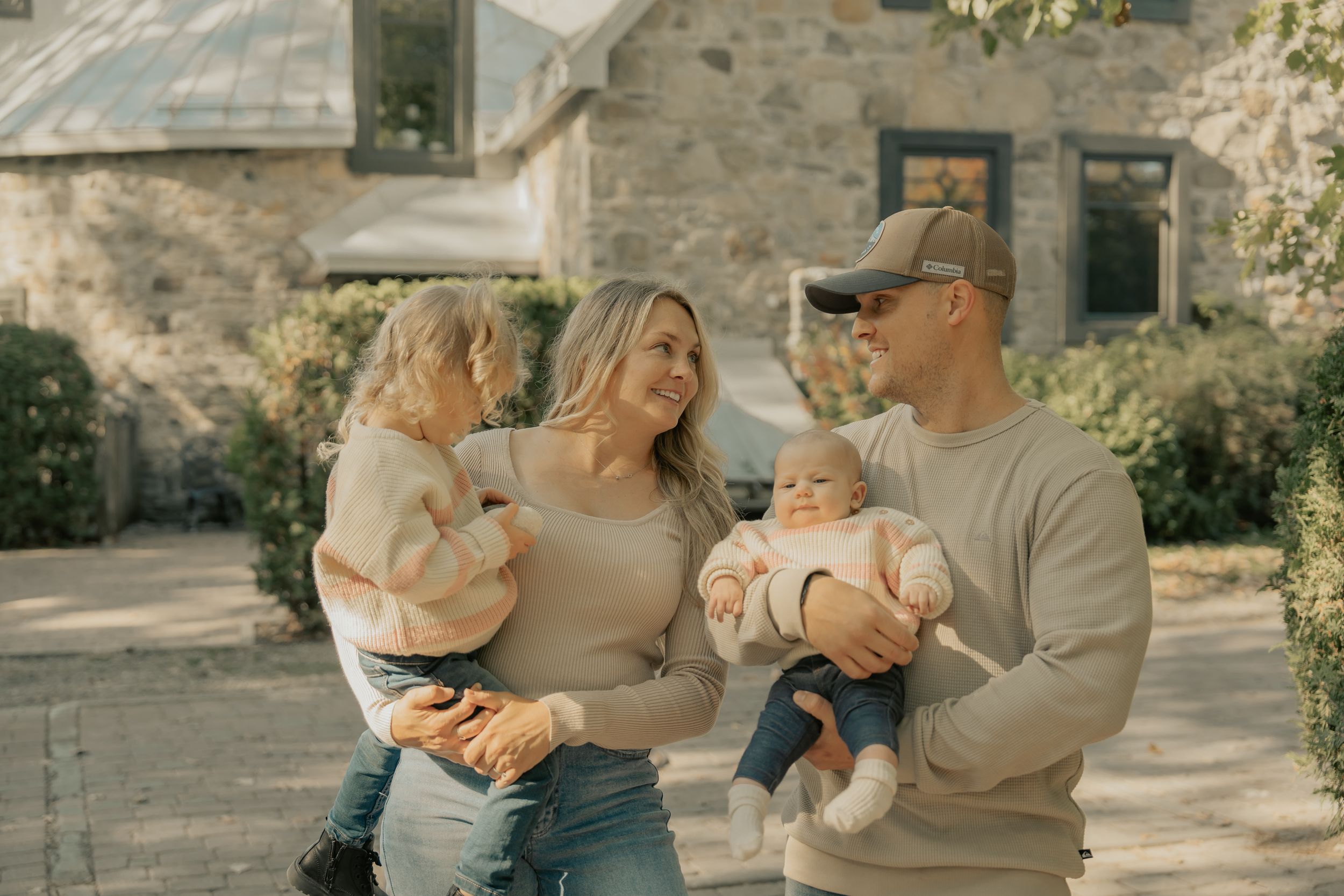 A family stands together on a sunny day outside a rustic stone house during a warm autumn afternoon.