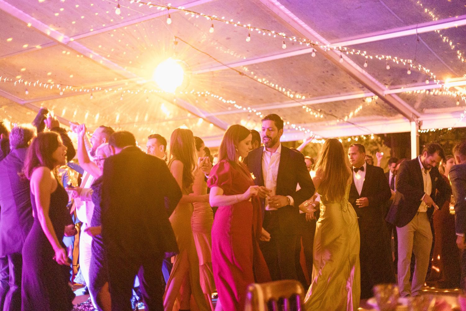 Wedding celebration under a tent with twinkling lights creating a magical atmosphere.