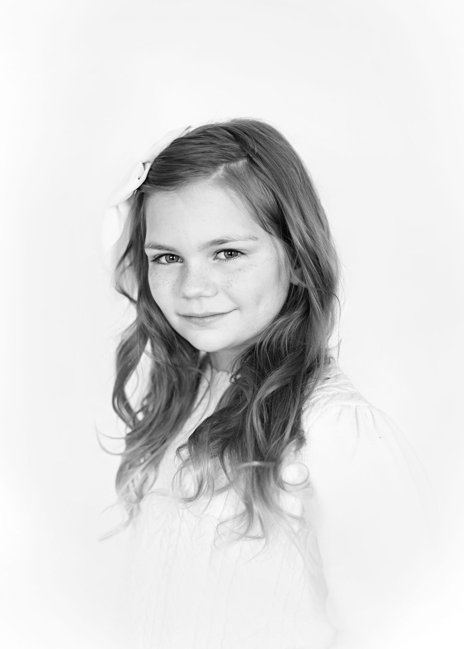 Black and white portrait of a young child with wavy hair and a gentle smile against a light background.