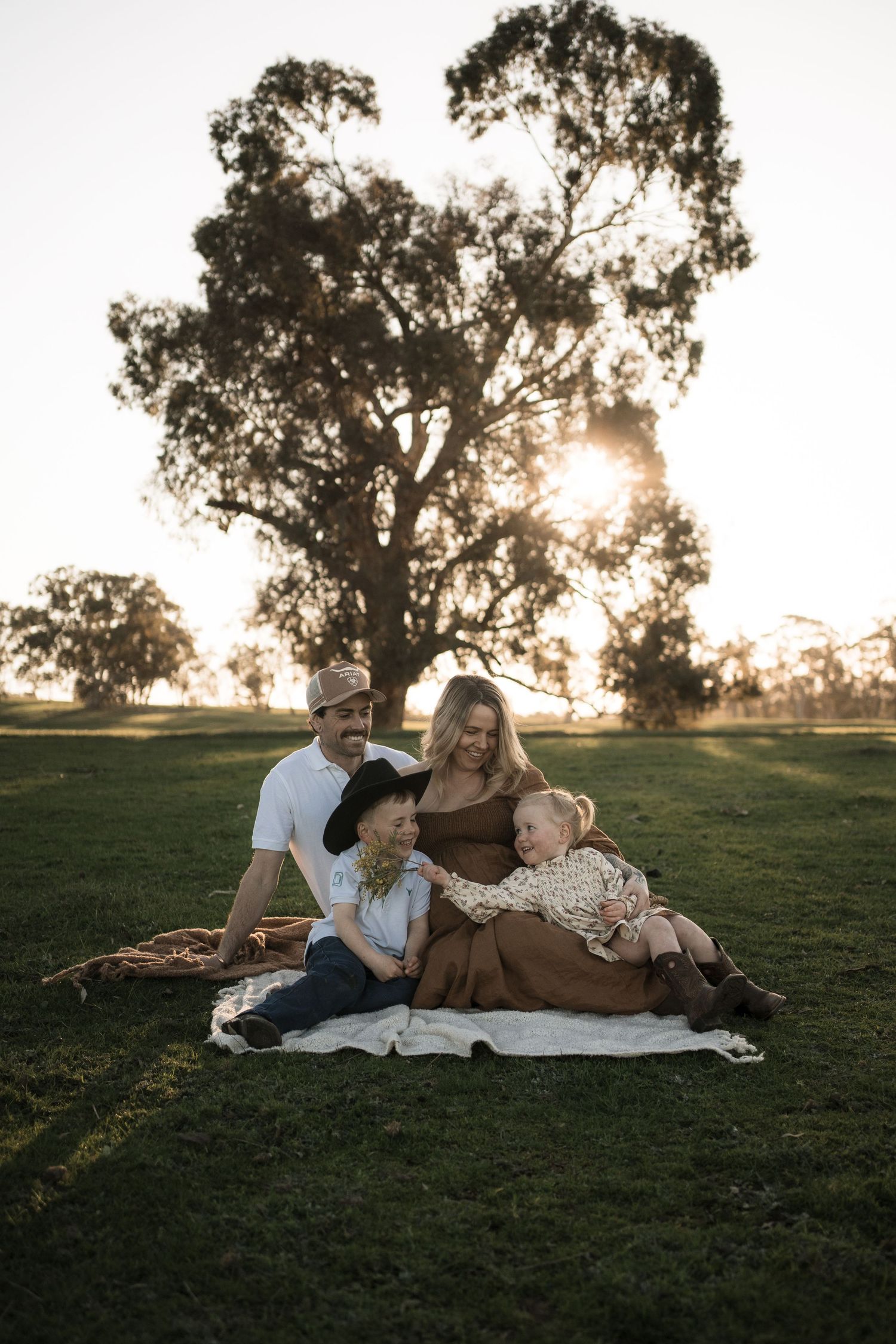 Family relaxing together on blanket in grassy field at sunset during outdoor photoshoot in Mansfield
