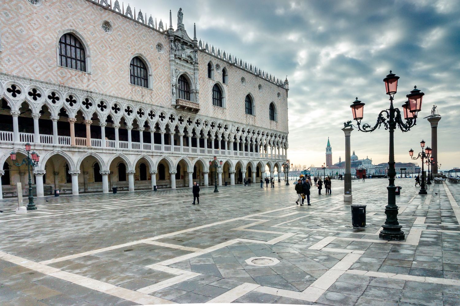 St. Mark's Square in Venice with the Doge's Palace reflected in floodwater under dramatic cloudy skies at dusk.