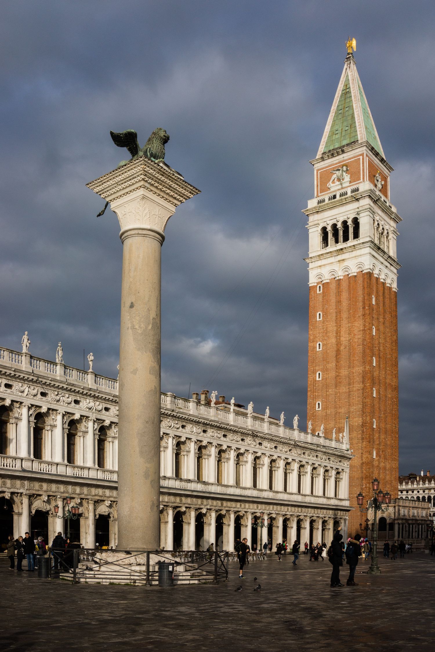 St Mark's Campanile and marble columns frame the historic Piazza San Marco in Venice under dramatic stormy skies.