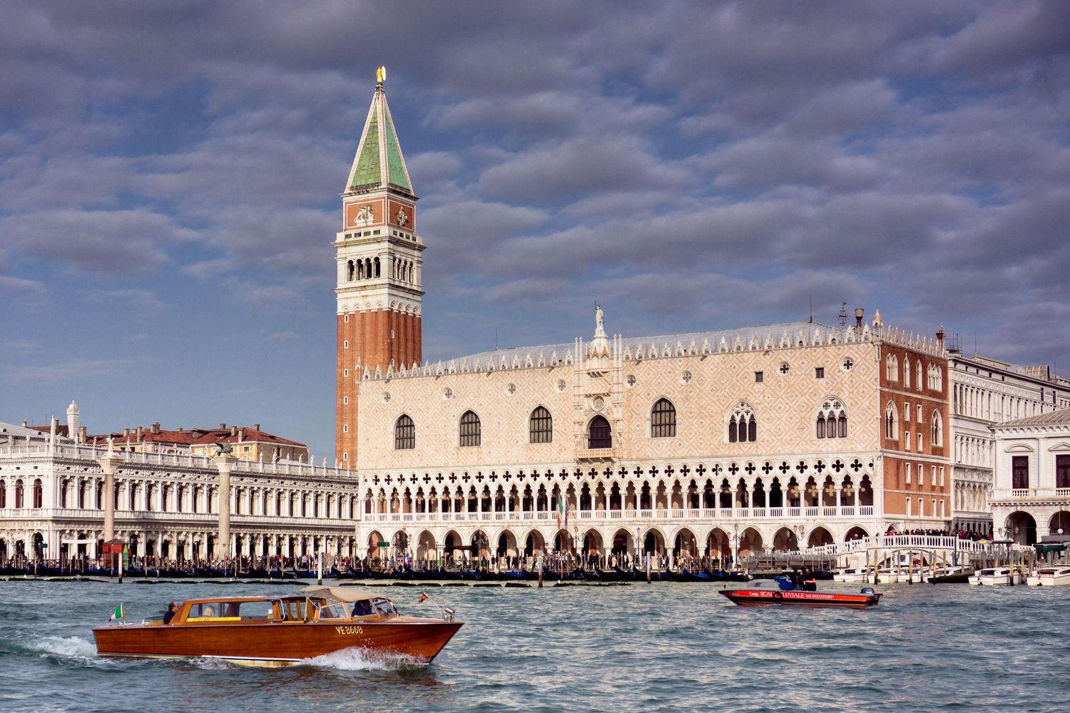 Panoramic cityscape of Venice waterfront with St Mark's Square and Doge's Palace under dramatic cloudy sky.