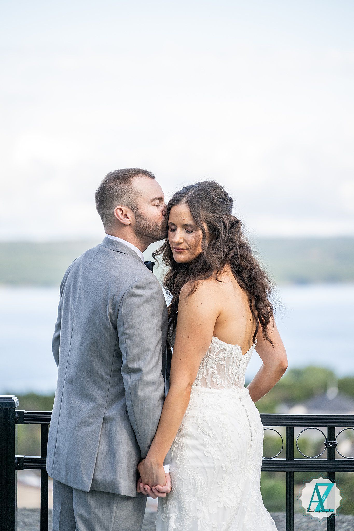 Romantic couple in wedding attire embrace on a scenic waterfront balcony during an intimate photo session.