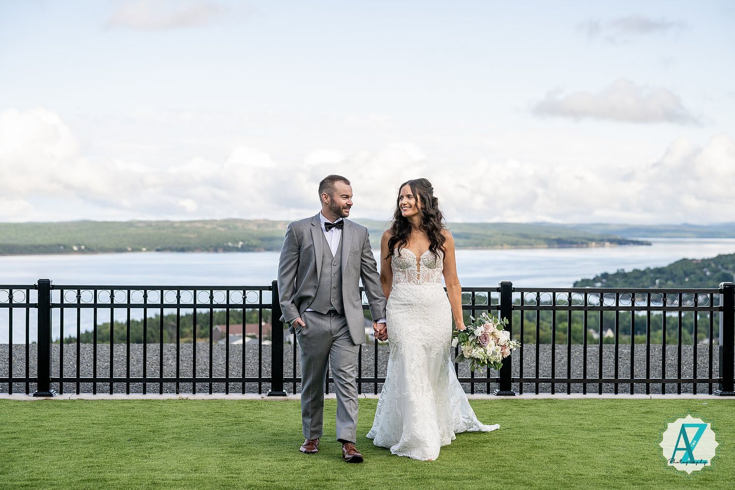 A couple shares a romantic moment on a hilltop overlooking the ocean during their wedding celebration.