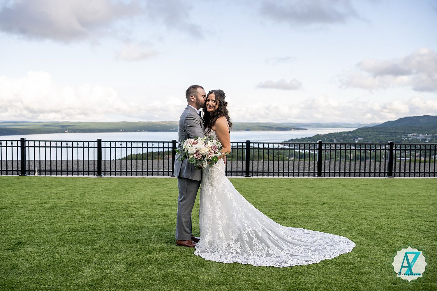Elegant wedding couple standing on a scenic green hilltop overlooking mountains with dramatic clouds in the background.