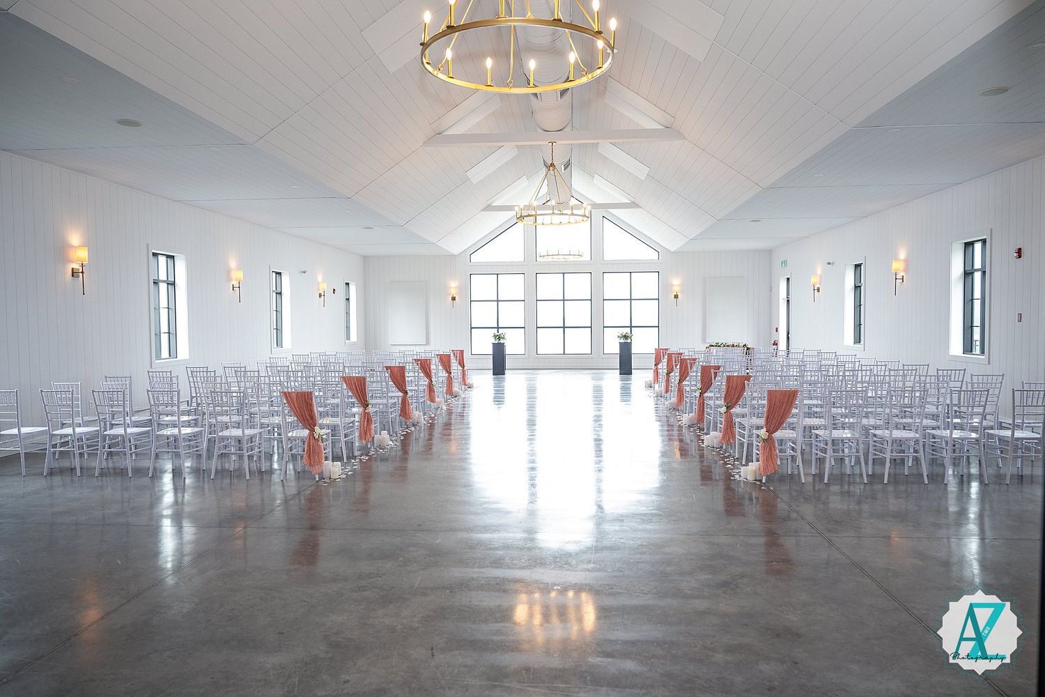 Modern event venue with white walls, circular chandelier, and rows of orange chairs arranged in a spacious indoor setting.