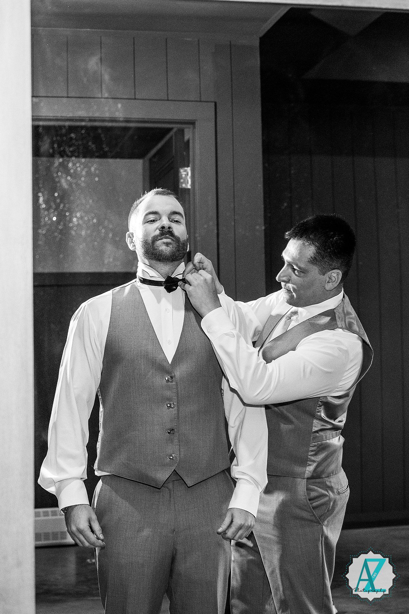A group of groomsmen in grey vests share a candid moment and laugh together in black and white.