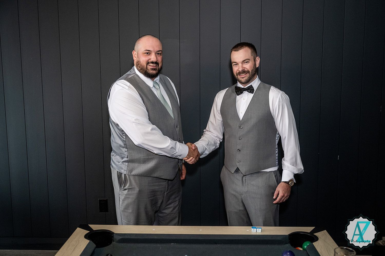 Three groomsmen in matching gray vests share candid moments and laughter against a dark background.