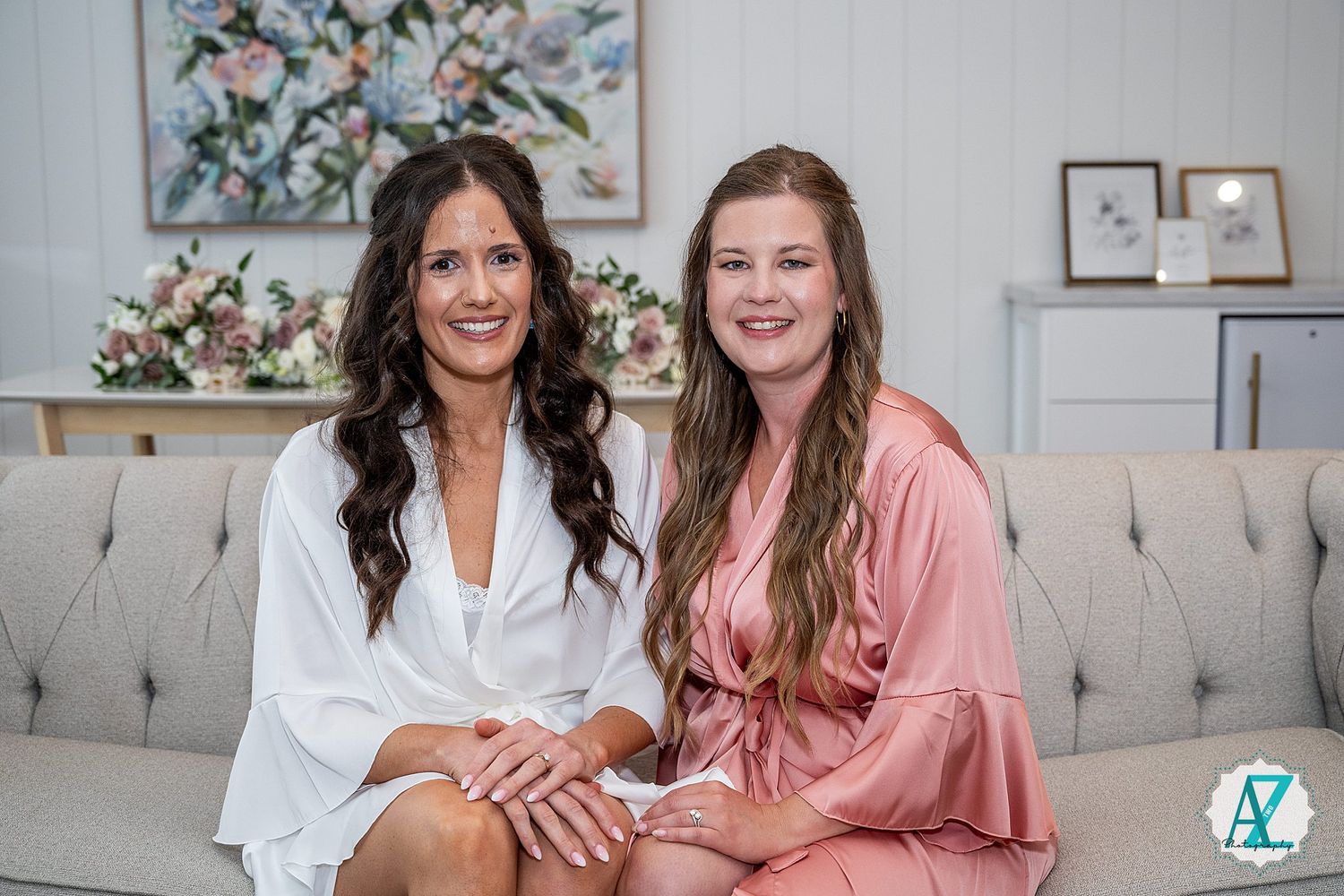 Two people sitting on gray couch for formal photos in contrasting white and pink outfits.