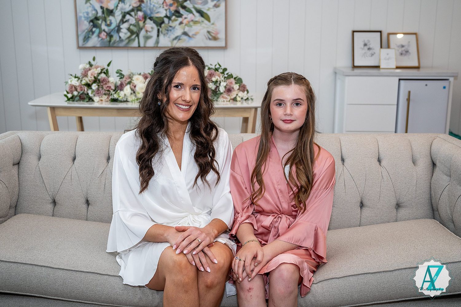 Two people in white and pink sitting on gray couch for pre-wedding photos.