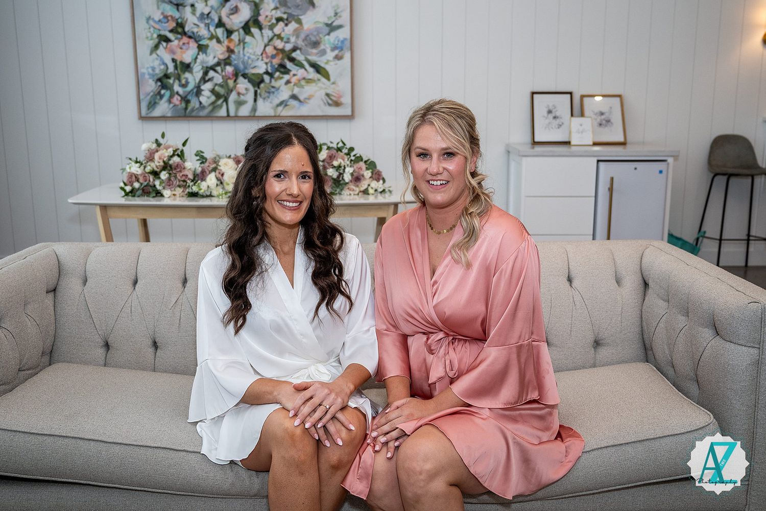 Two people laughing and posing on gray couch in white and pink outfits.