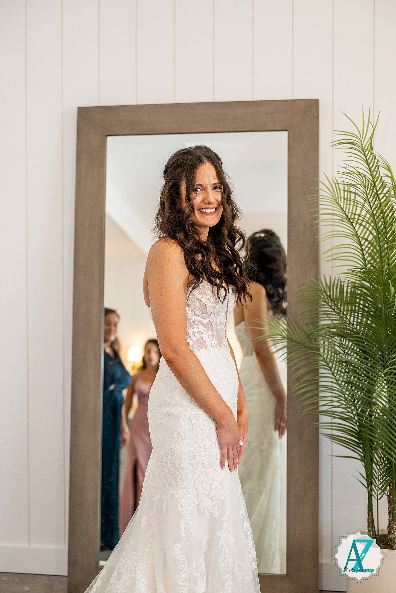 Wedding dress fitting in a bright room with wooden-framed mirrors and tropical plants in the background.