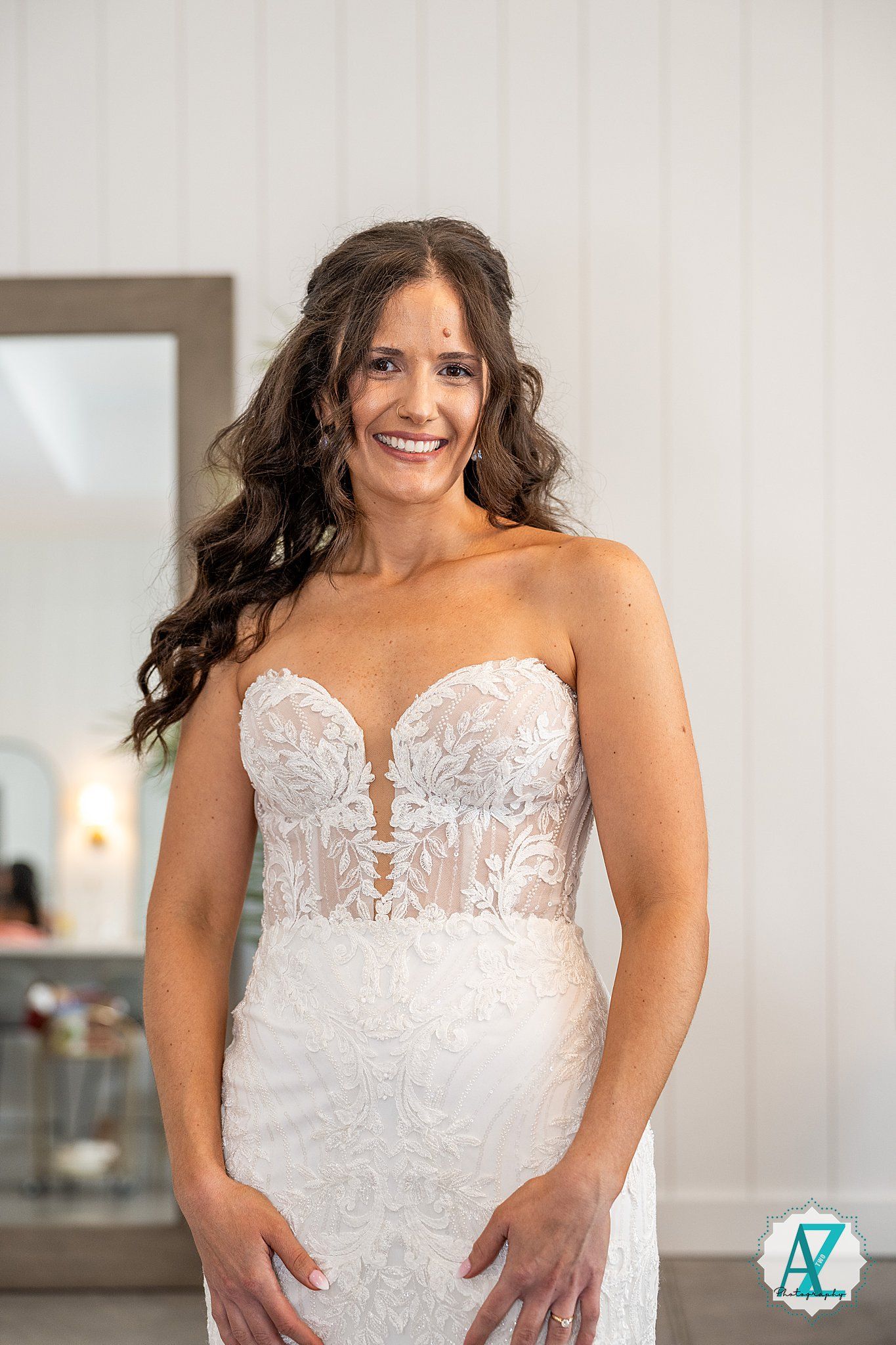 A bride poses joyfully in a detailed white lace wedding gown with a sweetheart neckline.