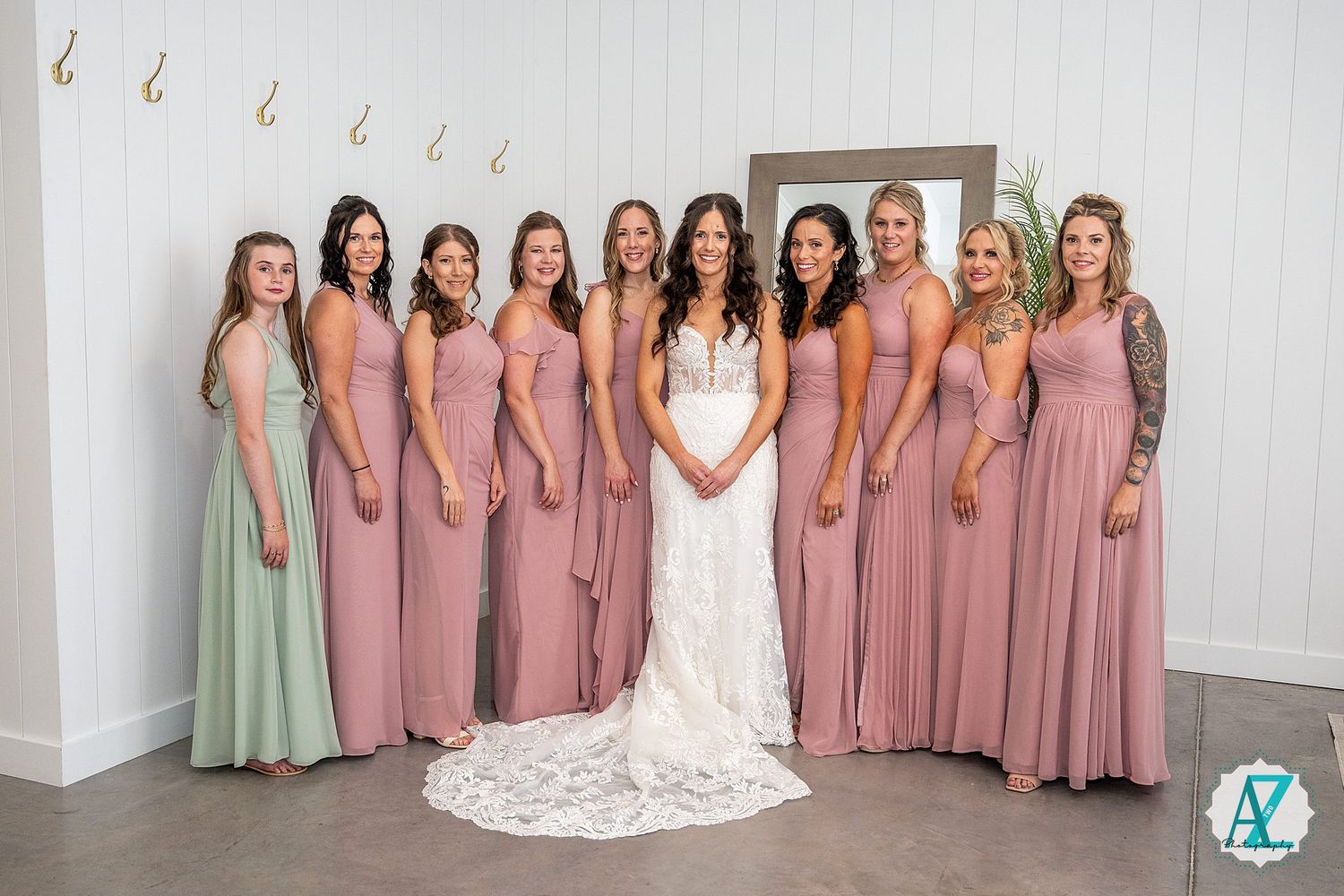 Wedding party poses for formal group photo with bridesmaids in mauve dresses and bride in white gown.