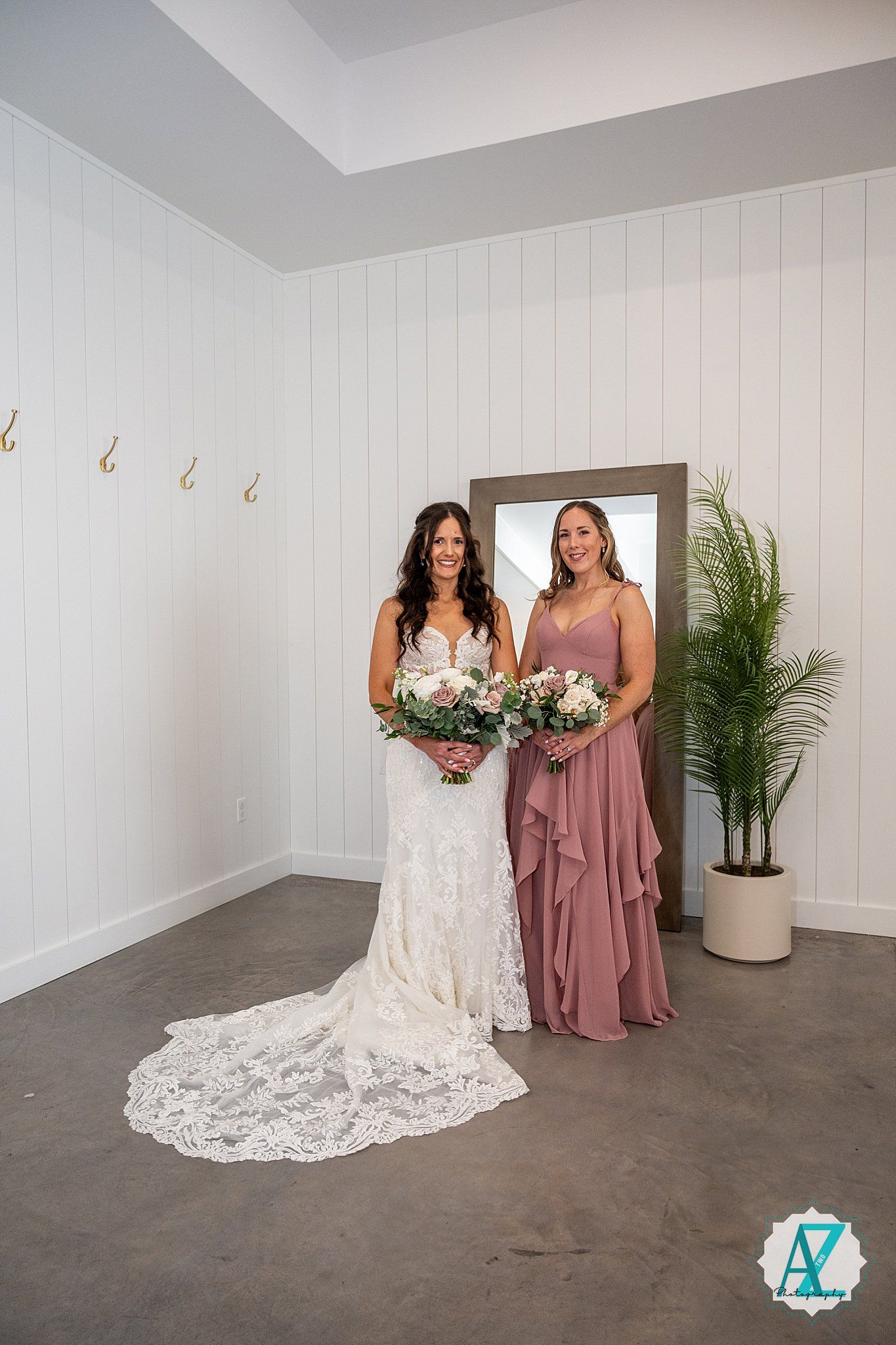 Two figures in a bridal suite, one wearing a white lace wedding gown and another in a dusty rose bridesmaid dress.