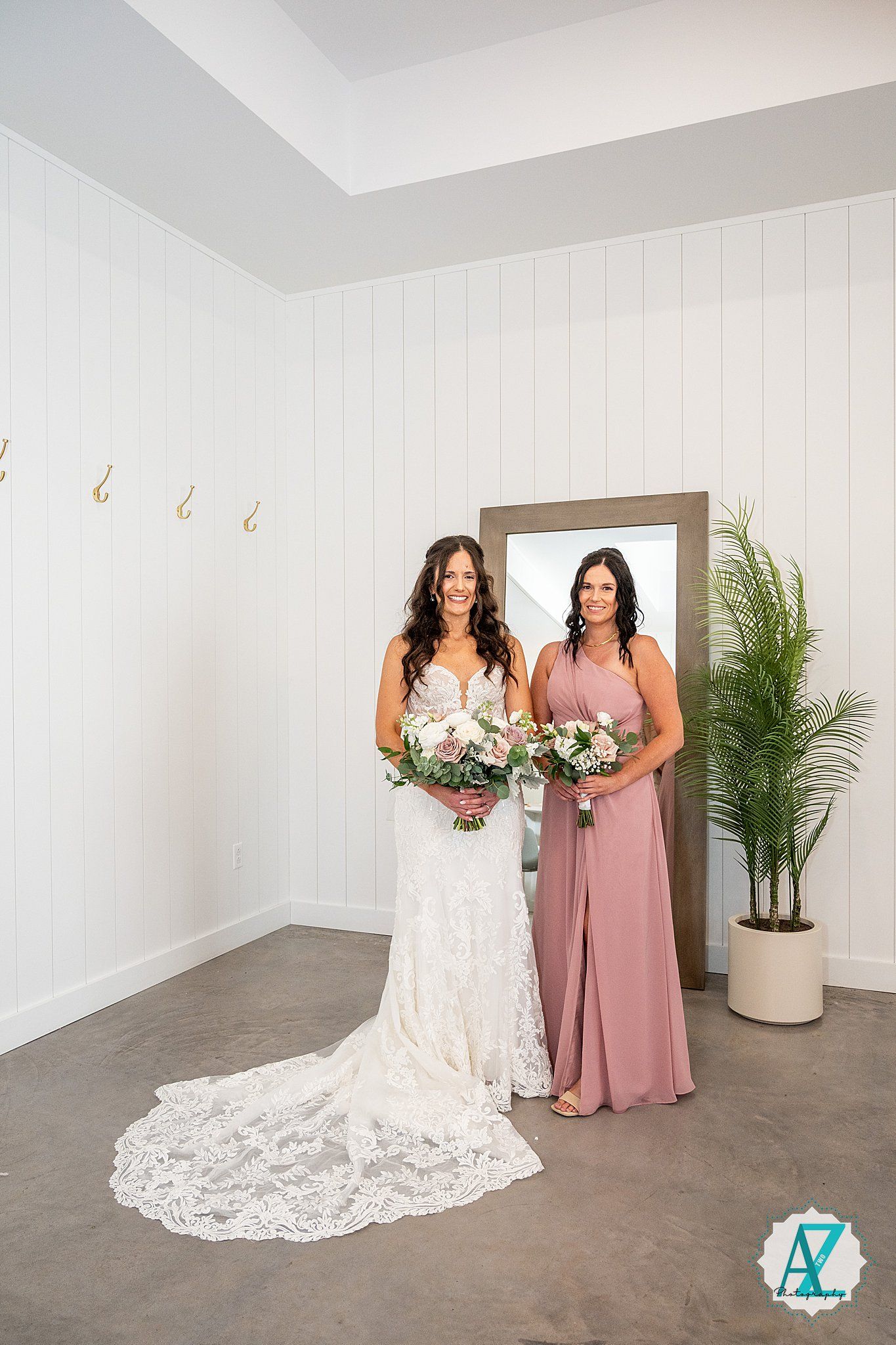 Bridal party members in white lace and dusty rose dresses pose together in a minimalist white studio setting.