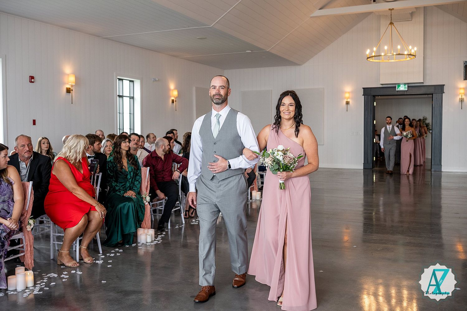Wedding guests gathered in an elegant reception hall with chandelier lighting and white chairs.