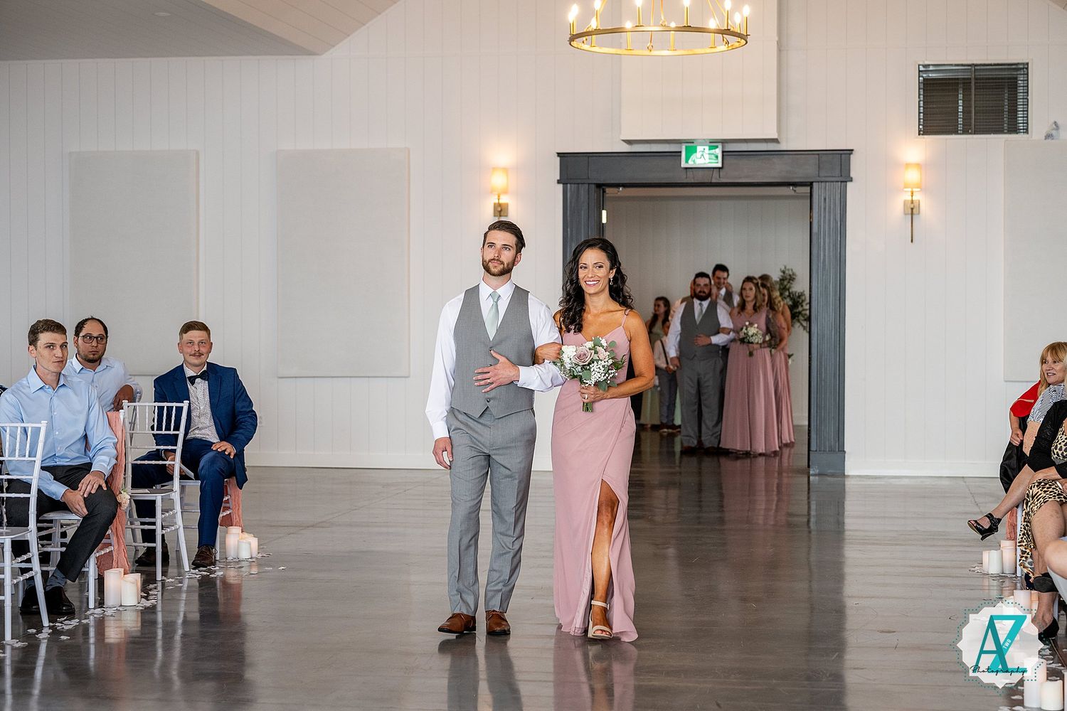 Wedding attendees dance and mingle in an elegant white ballroom with chandeliers during a reception celebration.